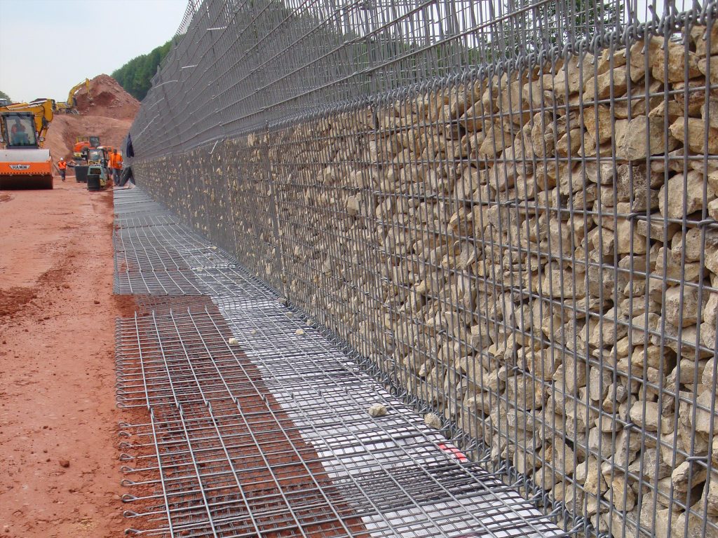 Bau einer Gabionen­wand mit Stahlgitter­elementen und Steinschüttung auf einer grossen Infrastruktur­baustelle.